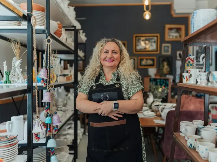 Smiling shop owner stands among shelves of ceramics, representing local retailers promoted by City Directory Spot